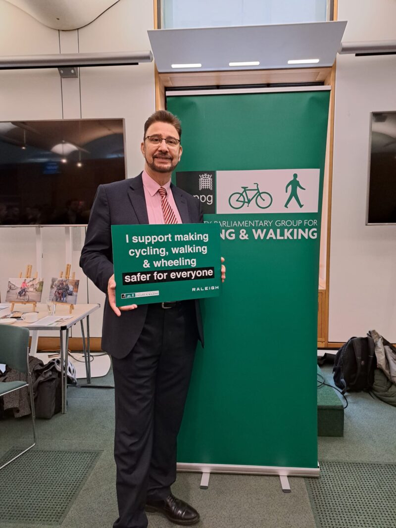 Afzal holding a sign that says "I support making cycling, walking and wheeling safer for everyone." 